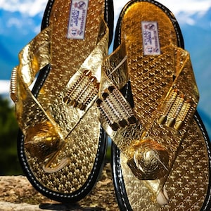 May include: A pair of gold leather sandals with black straps and a black sole. The sandals have a textured surface and are decorated with gold beads. The sandals are size 41.