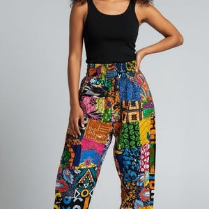 May include: A black sleeveless tank top paired with loose-fitting, high-waisted pants featuring a vibrant, multi-colored patchwork pattern. The pants have an elasticized waistband and gathered elastic cuffs at the ankles, showcasing various geometric and floral prints in shades of blue, yellow, pink, and green.