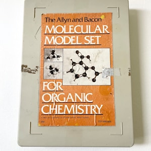 May include: A gray plastic box with a label that reads "The Allyn and Bacon Molecular Model Set for Organic Chemistry". The label has a picture of a molecular model and the text "1984 by Allyn and Bacon, Inc. All rights reserved. Made in England. EDP 688136X".