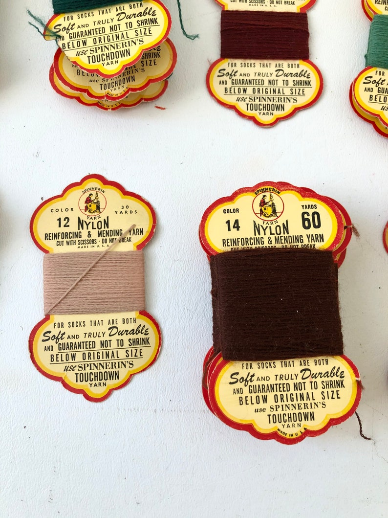 May include: Close-up of vintage nylon yarn spools in various colors. The spools have red and yellow labels with text that reads "Soft and Truly Durable" and "Spinnerin's Touchdown Yarn". The yarn colors include brown, tan, and green.
