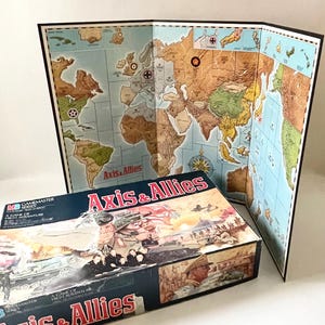 May include: A vintage board game titled "Axis & Allies" with a world map game board. The box features illustrations of military vehicles and soldiers. The game board is open, displaying a detailed map of the world with various territories.