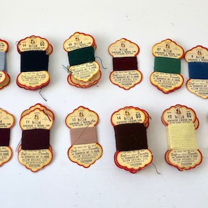 May include: A collection of vintage nylon reinforcing and mending yarn spools in various colors, including blue, black, green, burgundy, and red. Each spool is labeled with a color number and the text "Nylon 60".