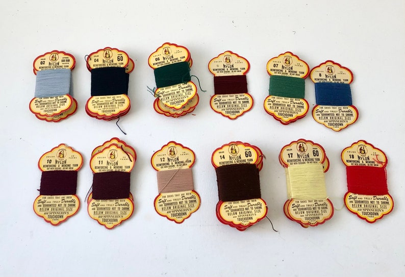 May include: A collection of vintage nylon reinforcing and mending yarn spools in various colors, including blue, black, green, burgundy, and red. Each spool is labeled with a color number and the text "Nylon 60".