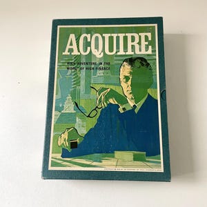 Pode incluir: Uma caixa azul com a palavra "ACQUIRE" em letras brancas. A caixa tem um fundo verde com uma cidade e um homem de terno olhando para um monte de cartas. O texto "HIGH ADVENTURE IN THE WORLD OF HIGH FINANCE" está abaixo da palavra "ACQUIRE".
