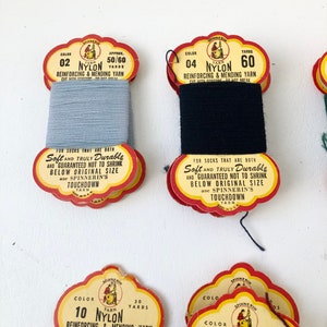 May include: Spools of vintage nylon yarn in various colors. The labels read "Reinforcing & Mending Yarn" and "Soft and Truly Durable." The colors include light blue and black. The labels are red and yellow.