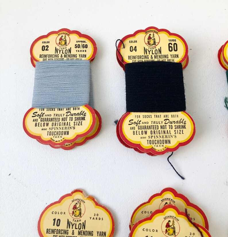 May include: Spools of vintage nylon yarn in various colors. The labels read "Reinforcing & Mending Yarn" and "Soft and Truly Durable." The colors include light blue and black. The labels are red and yellow.