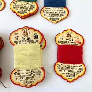 May include: Close-up of several spools of nylon yarn in various colors, including green, blue, yellow, and red. Each spool has a vintage label with text that reads "Soft and Truly Durable" and "Touchdown Yarn".
