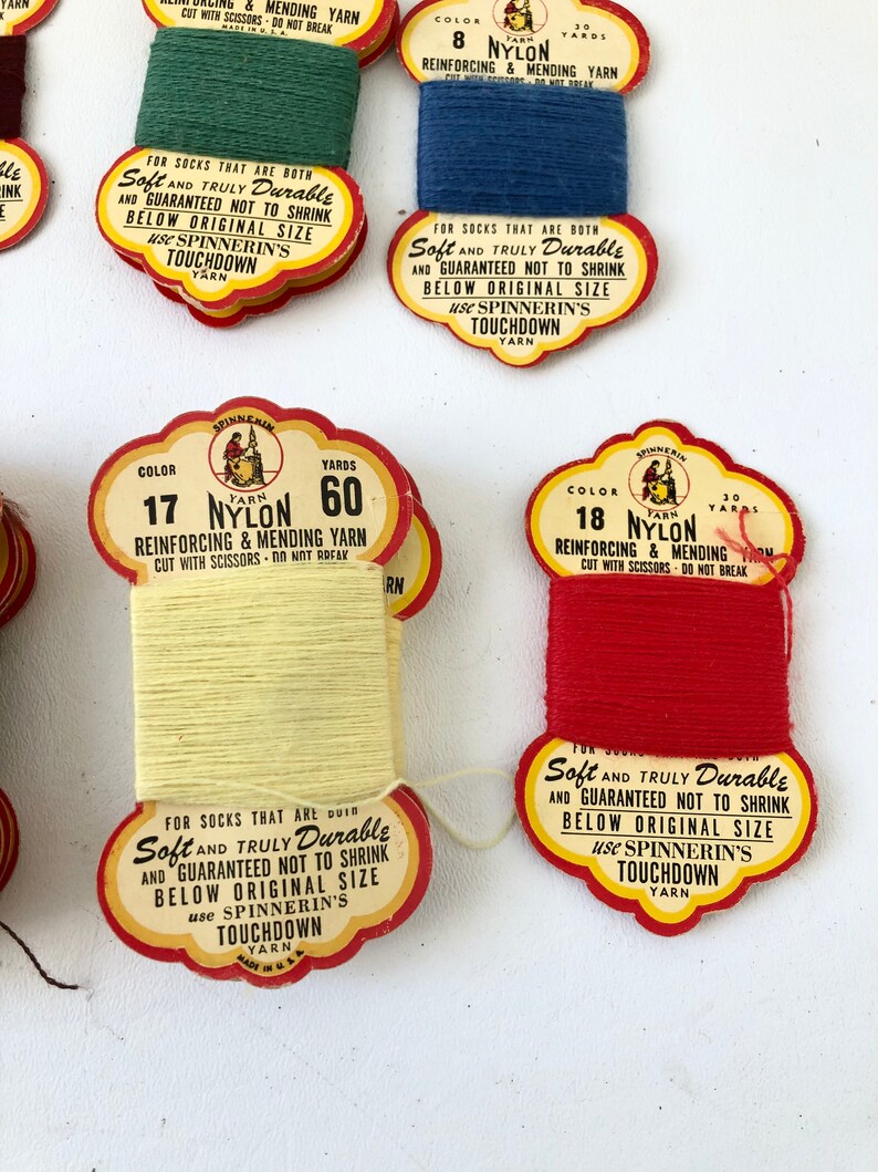 May include: Close-up of several spools of nylon yarn in various colors, including green, blue, yellow, and red. Each spool has a vintage label with text that reads "Soft and Truly Durable" and "Touchdown Yarn".