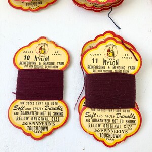 May include: Vintage spools of nylon yarn in shades of burgundy and blue-grey. Each spool has a decorative label with text that reads "Soft and Truly Durable" and "Touchdown Yarn". Ideal for reinforcing and mending socks.