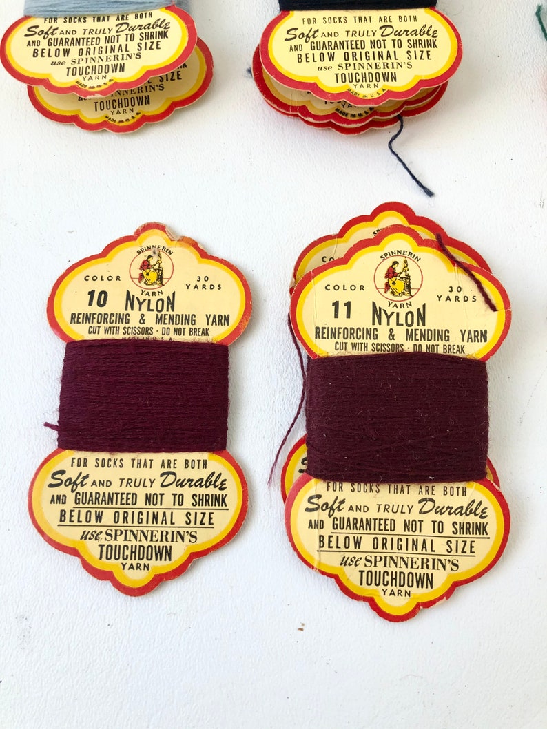 May include: Vintage spools of nylon yarn in shades of burgundy and blue-grey. Each spool has a decorative label with text that reads "Soft and Truly Durable" and "Touchdown Yarn". Ideal for reinforcing and mending socks.