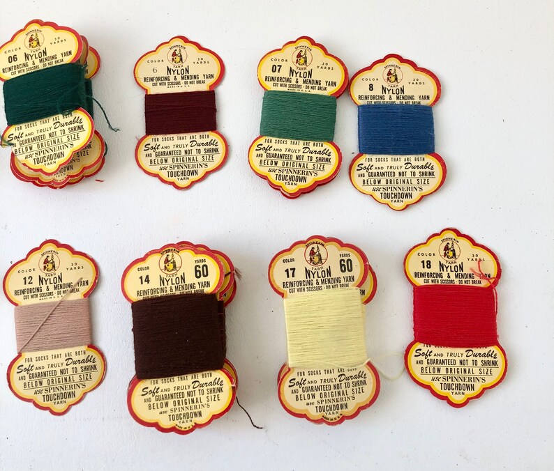 May include: A collection of eight spools of nylon yarn in various colors, including green, burgundy, teal, blue, tan, brown, yellow, and red. Each spool has a vintage label with text.