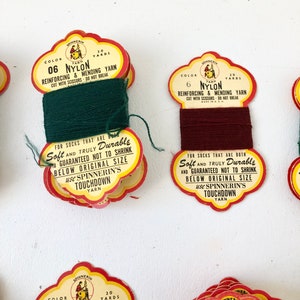 May include: Close-up of several vintage spools of nylon yarn. Each spool has a colorful label with text that reads "Reinforcing & Mending Yarn" and "Soft and Truly Durable". The yarn colors include green and burgundy.