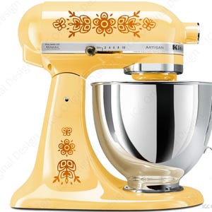 May include: A yellow Artisan stand mixer with floral decals. The mixer has a stainless steel mixing bowl and a speed control dial. The text "ARTISAN" and "Kit" are visible on the mixer.