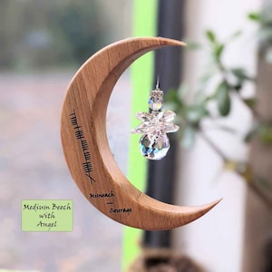 May include: A wooden crescent moon with a crystal angel hanging from it. The moon is engraved with the word "Courage" and the runic symbol for "Misneach", which means courage in Irish.