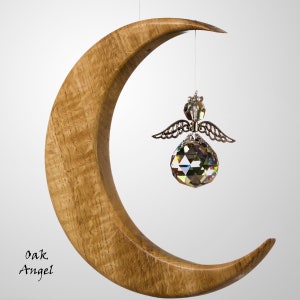 May include: A wooden crescent moon with a light brown finish, holding a crystal angel ornament. The angel has silver wings and a faceted crystal body. The text "Oak Angel" is printed on the bottom left.