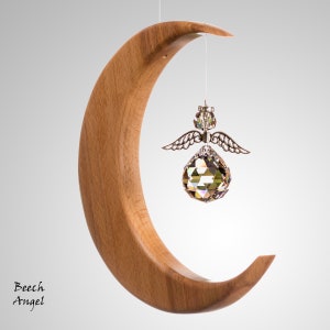 May include: A wooden crescent moon with a crystal angel pendant. The moon is made of light brown wood. The angel has silver wings and a faceted crystal body. Text on the bottom left says "Beech Angel".