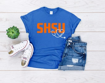 Könnte beinhalten: Ein königsblaues T-Shirt mit dem Text "SHSU nurse" in Orange und Weiß. Der Text "nurse" befindet sich in einem Herz mit einem Stethoskop.