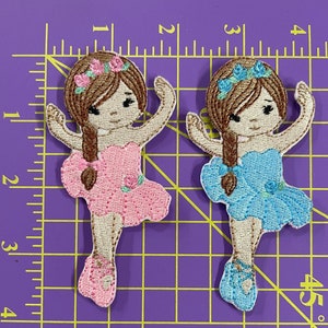 May include: Two embroidered iron-on patches of ballerinas. One ballerina is wearing a pink tutu and the other is wearing a blue tutu. Both ballerinas have brown hair and a flower crown.