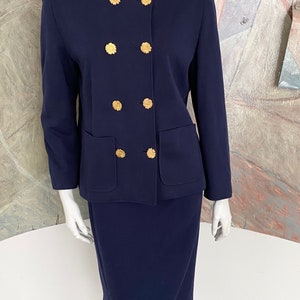 May include: A navy blue skirt suit with a double-breasted jacket featuring gold flower-shaped buttons.