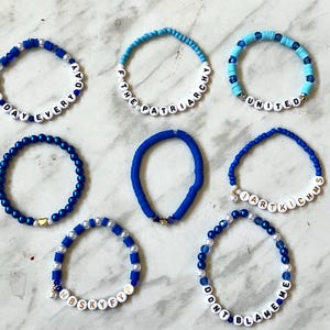 May include: Nine blue and white beaded bracelets with different messages, including "All Day Every Day", "F The Patriarchy", "United", "I Art Kichms", "Don't Blame Me", and "Nbskyfy".