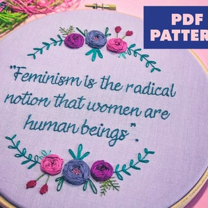 Puede incluir: Un aro de bordado morado con una cita que dice "El feminismo es la idea radical de que las mujeres son seres humanos." La cita est&aacute; rodeada de una corona de hojas verdes y flores rosas y moradas.