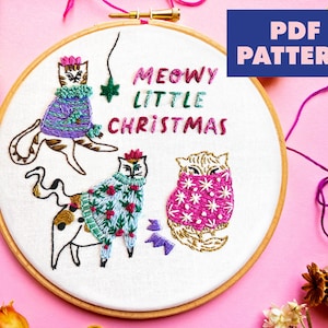 May include: Embroidered hoop art featuring three cats wearing festive sweaters. The cats are surrounded by the text "MEOWY LITTLE CHRISTMAS".