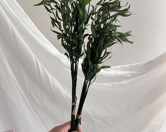 Op de afbeelding: Een bundel kunstmatige groene wilgentakken met lange, smalle en puntige bladeren. De stelen zijn donkergroen en samengebonden met een dun, lichtbruin touwtje. Het blad heeft een natuurlijke, licht gebogen vorm en een diepgroene kleur.