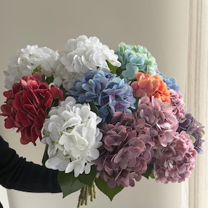 May include: A bouquet of colorful faux hydrangeas in shades of red, white, blue, green, orange, and purple. The flowers are clustered together with green leaves and stems, creating a vibrant and eye-catching arrangement.
