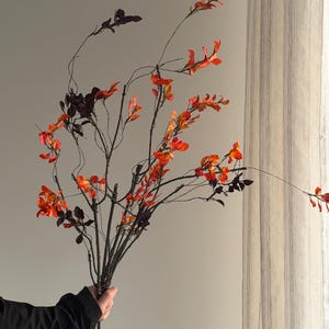 Peut inclure: Un bouquet de branches artificielles avec des feuilles orange vif et rouge foncé. Les branches sont maintenues ensemble, créant une esthétique automnale naturelle. Les feuilles présentent un dégradé de couleurs, ajoutant de la profondeur et de l'intérêt visuel à l'arrangement.