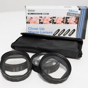 May include: A Vivitar 58mm 4-piece close-up macro lens kit including a black carrying case and four circular black lens filters. The white product box displays the text Vivitar, Series 1, 58mm 4 Piece Kit, and Close-Up Macro Lenses with images.