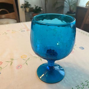 May include: A blue glass goblet with a textured surface. The goblet has a wide bowl and a tall stem.