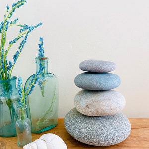 May include: A stack of gray and white stones, with a blue vase and a smaller clear glass vase filled with blue flowers. The vases are on a wooden surface.