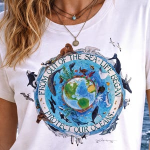 A white t-shirt with a graphic design depicting various marine animals and the Earth, along with the text "FROM OUT OF THE SEA LIFE BEGINS PROTECT OUR OCEANS".