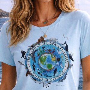 A woman wearing a light blue t-shirt with a graphic design depicting various marine animals and the Earth, along with the text "FROM OUT OF THE SEA LIFE BEGINS" and "PROTECT OUR OCEANS".