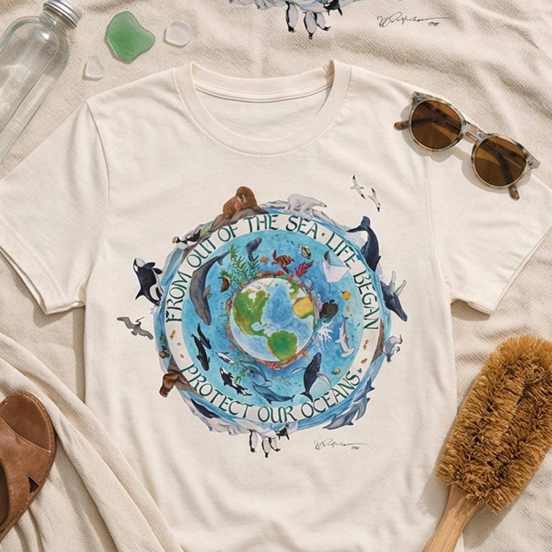 A white t-shirt with a graphic design depicting a globe surrounded by various marine life, along with the text "FROM OUT OF THE SEA LIFE BEGINS PROTECT OUR OCEANS".
