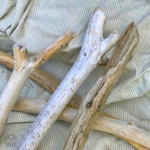 May include: Four pieces of driftwood, some painted white, arranged on a striped fabric background. The driftwood is natural and has a rustic look.