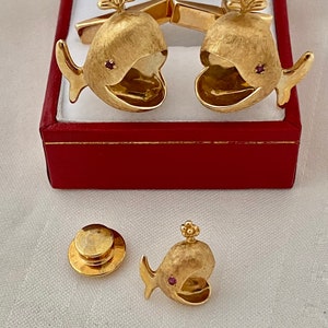 May include: Gold whale cufflinks and tie tack set with red gemstone accents. The cufflinks are in a red velvet box.