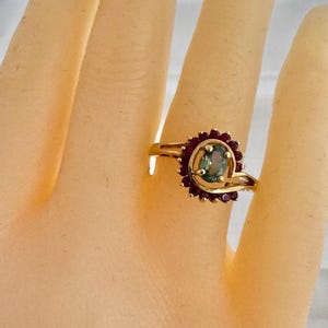 May include: A gold ring with a green gemstone surrounded by a halo of red rubies.