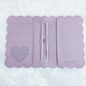 May include: A lavender-colored, scalloped-edge notebook cover with a heart-shaped window featuring a glittery star pattern. The cover has two white elastic straps and the text "The Honey & Hive" is printed on the right side.