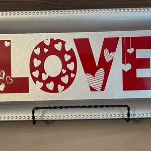 May include: A silver tray with a beaded border features a red vinyl decal of the word "LOVE" with hearts. The hearts are in various patterns and sizes.