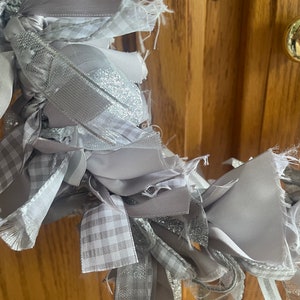 May include: A gray and white ribbon wreath with a gingham pattern. The wreath is made of multiple ribbons that are tied together and frayed at the edges.