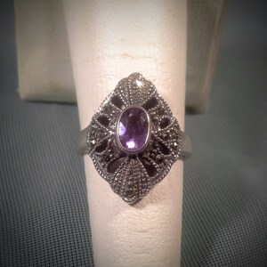 May include: A silver ring with a purple amethyst gemstone set in a filigree design.