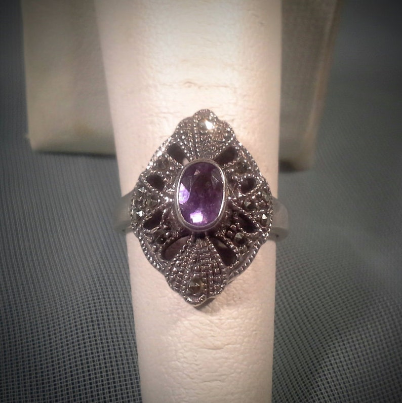 May include: A silver ring with a purple amethyst gemstone set in a filigree design.