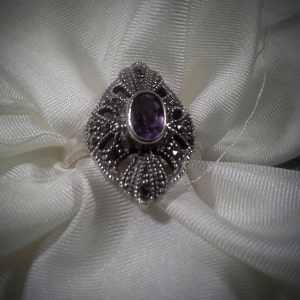 May include: A silver ring with a purple gemstone set in a filigree design.