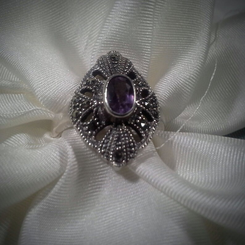 May include: A silver ring with a purple gemstone set in a filigree design.