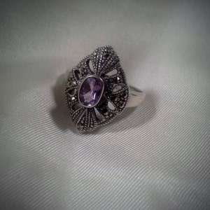 May include: A silver ring with a purple amethyst gemstone set in a detailed filigree design.