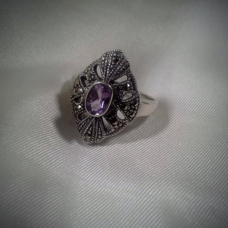 May include: A silver ring with a purple amethyst gemstone set in a detailed filigree design.