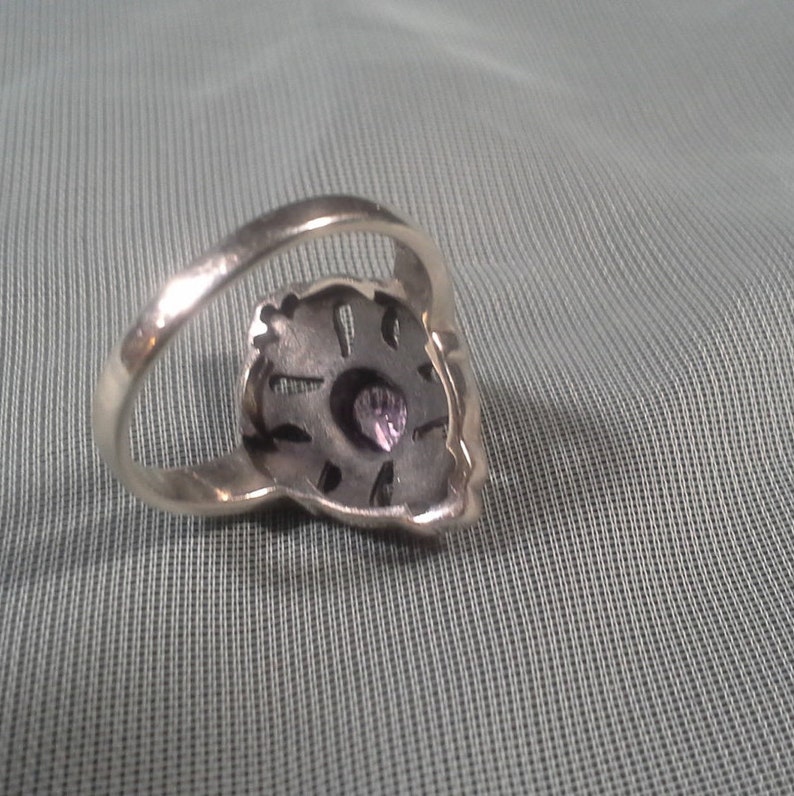 May include: A silver ring with a purple gemstone set in a detailed design.