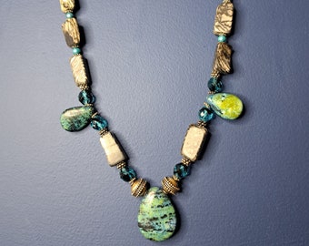 May include: A turquoise and green stone necklace with silver and gold accents. The necklace features a large teardrop-shaped pendant and smaller rectangular stones.
