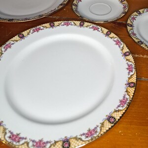 May include: A white porcelain dinner plate with a gold and black floral border. The plate has a delicate floral pattern with pink, purple, and blue accents.